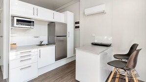 Una cocina moderna con armarios blancos, microondas integrado, refrigerador de acero inoxidable y una pequeña isla con una computadora portátil.