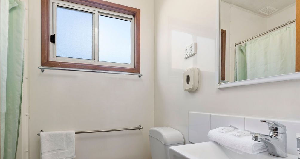Une salle de bain avec une fenêtre, un porte-serviettes, des toilettes, un lavabo et un miroir.