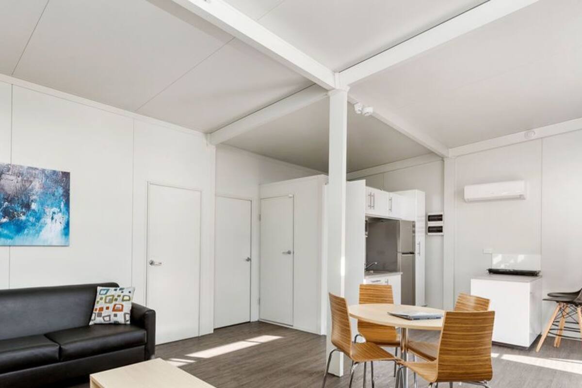 A modern living room with a black sofa, a dining table with chairs, and a kitchen area in the background.