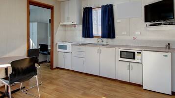 A compact kitchen with white cabinets, a microwave, a refrigerator, a sink, and a television mounted above the counter.