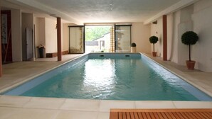 An indoor swimming pool with clear glass walls, a wooden deck in the foreground, and potted plants on the sides. - The closed Hellen .... (monterblanc)