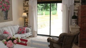 A rustic room with a stone wall, a wooden ceiling, a large window, a sofa, a chair, and a table with a vase of flowers. - The closed Hellen .... (monterblanc)