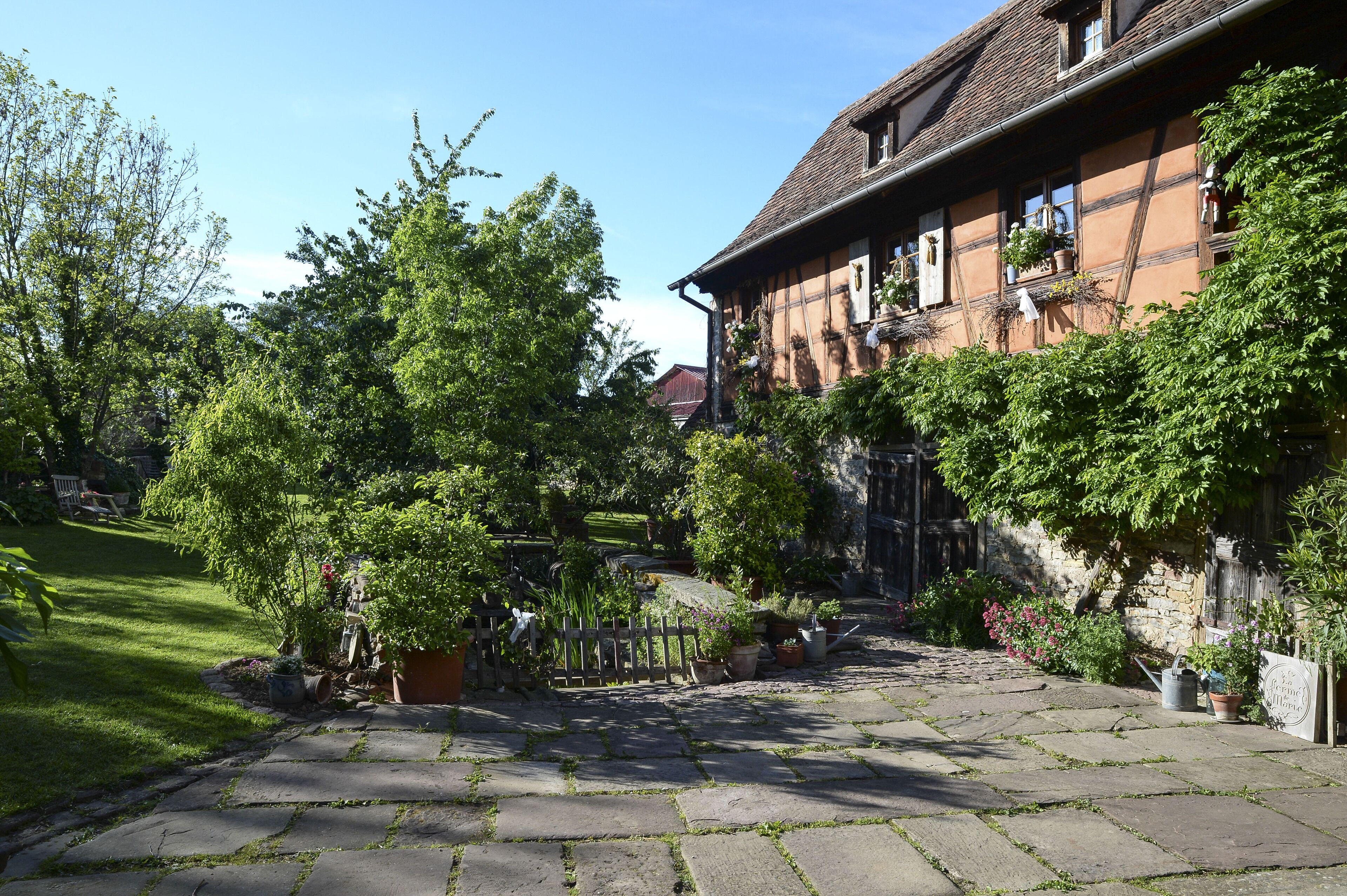 A traditional half-timbered house with a stone pathway leading to the entrance, surrounded by lush greenery and potted plants.