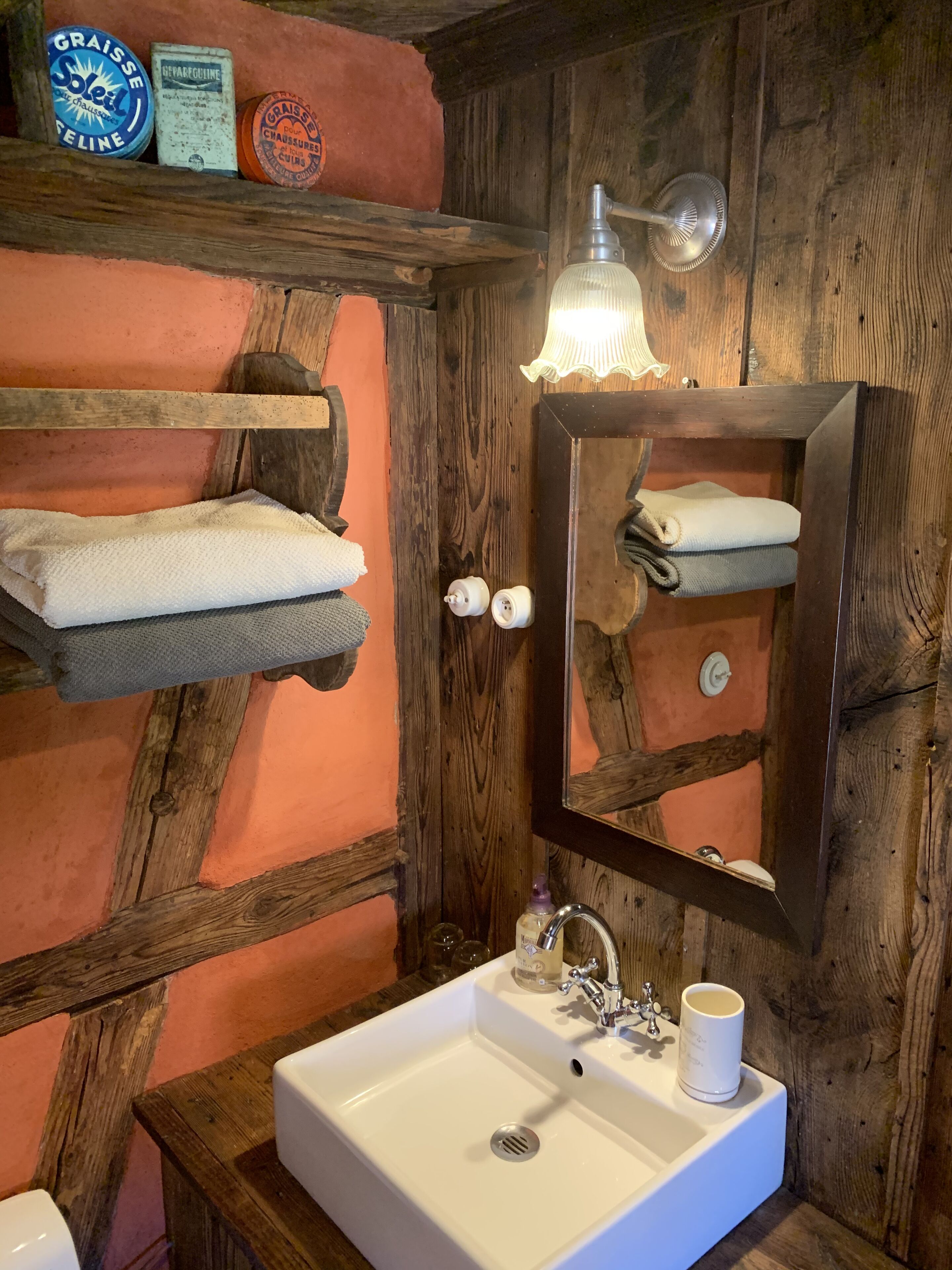 Une salle de bain rustique avec un mur en bois, un lavabo blanc et un miroir au-dessus.