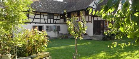 A traditional half-timbered house with a stone wall and a small tree in the foreground.