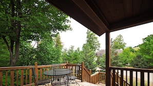 Une terrasse en bois avec une table et des chaises, entourée d’arbres et offrant une vue sur une colline.
