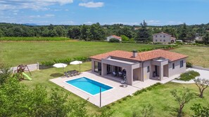 A modern two-story house with a swimming pool, surrounded by a well-maintained lawn and trees.