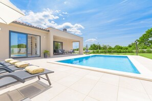 A modern house with a swimming pool, outdoor seating, and a glass door leading to a pool area.