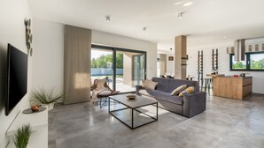 Ein modernes Wohnzimmer mit Sofa, Couchtisch und Fernseher. Ein Schiebetür aus Glas führt zu einem Balkon.