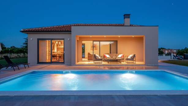 Ein modernes Haus mit Swimmingpool, einer Terrasse mit Gartenmöbeln und einem gut beleuchteten Innenraum.