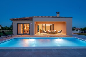 Una casa moderna con piscina, un patio con mobiliario exterior e interior luminoso.