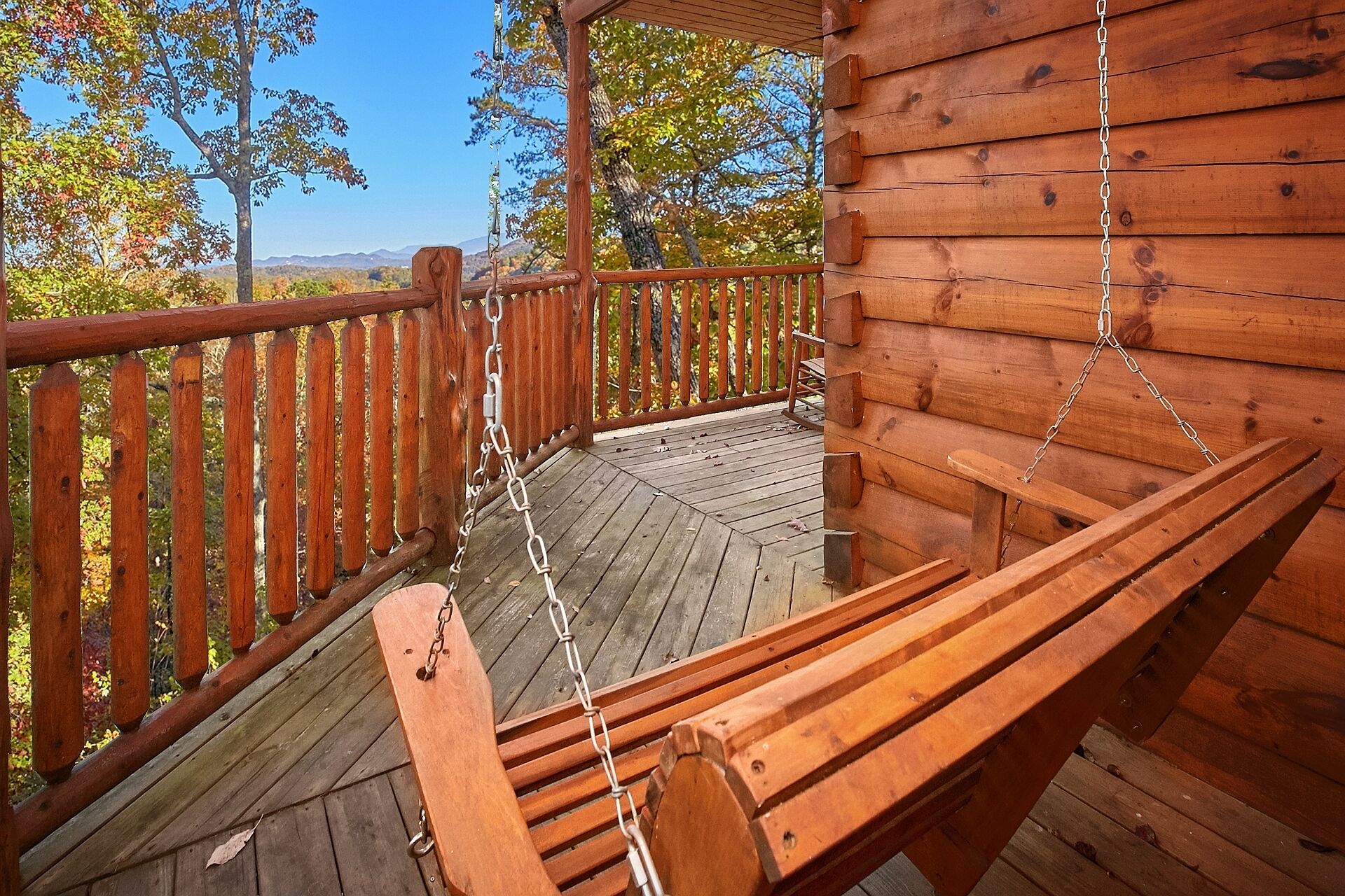 A wooden deck with a swing chair, a wooden bench, and a view of trees and mountains.