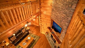 A log cabin interior with a stone fireplace, wooden walls, and a cozy seating area with a fireplace. - Family Adventure Cabin | Large theater | Views (Sevierville)