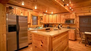 A wooden cabin-style kitchen with a central island, stainless steel refrigerator, and a microwave. - Family Adventure Cabin | Large theater | Views (Sevierville)