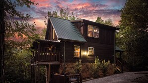 A rustic cabin with a stone foundation, a wooden deck, and a staircase leading to the entrance. - Indoor Pool Cabin  | Romantic | Sleeps 4 (Sevierville)