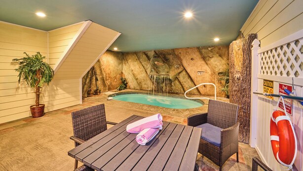 An indoor pool area with a waterfall feature, wicker furniture, and a lifebuoy on a fence. - Indoor Pool Cabin  | Romantic | Sleeps 4 (Sevierville)