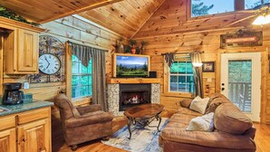 A cozy cabin interior with wooden walls, a stone fireplace, a television, and a dining area. - Indoor Pool Cabin  | Romantic | Sleeps 4 (Sevierville)