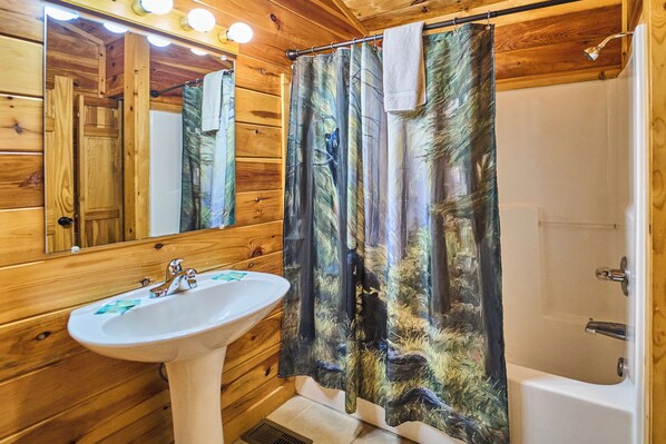 A wooden cabin bathroom with a white sink, a shower, and a forest-themed shower curtain. - Indoor Pool Cabin | Romantic | Sleeps 4 (Sevierville)