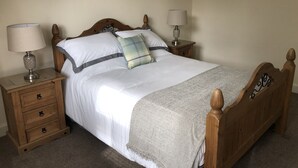 Un lit bien fait, avec du linge de lit blanc, un coussin à carreaux et un plaid gris. Il y a deux tables de chevet avec des lampes et une table de nuit en bois avec des tiroirs.