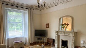 Un salon avec une cheminée, un téléviseur et une grande fenêtre avec des rideaux.