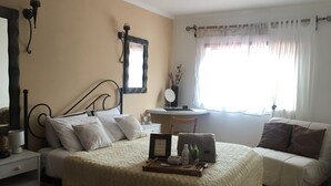 Une chambre à coucher avec un lit, une table de chevet, une chaise, un bureau et une fenêtre avec des rideaux.