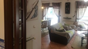 Un salon avec un canapé, une table à manger et une chaise. Il y a un tableau au mur et une fenêtre avec des rideaux.