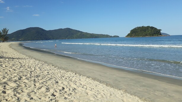 A beach with a clear sky, a sandy shore, and a small island in the distance.