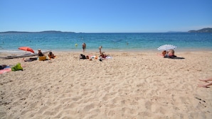 A beach with people sunbathing and swimming, a boat, and umbrellas. - Apartment near the sea (Hyères)