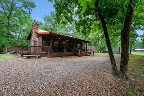 A cabin with a stone chimney, a porch, and a gravel driveway.