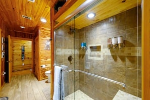 A wooden interior with a glass-enclosed shower, tiled walls, and a visible toilet.