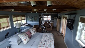 A bedroom with a large bed, a desk, a chair, and a kitchenette.
