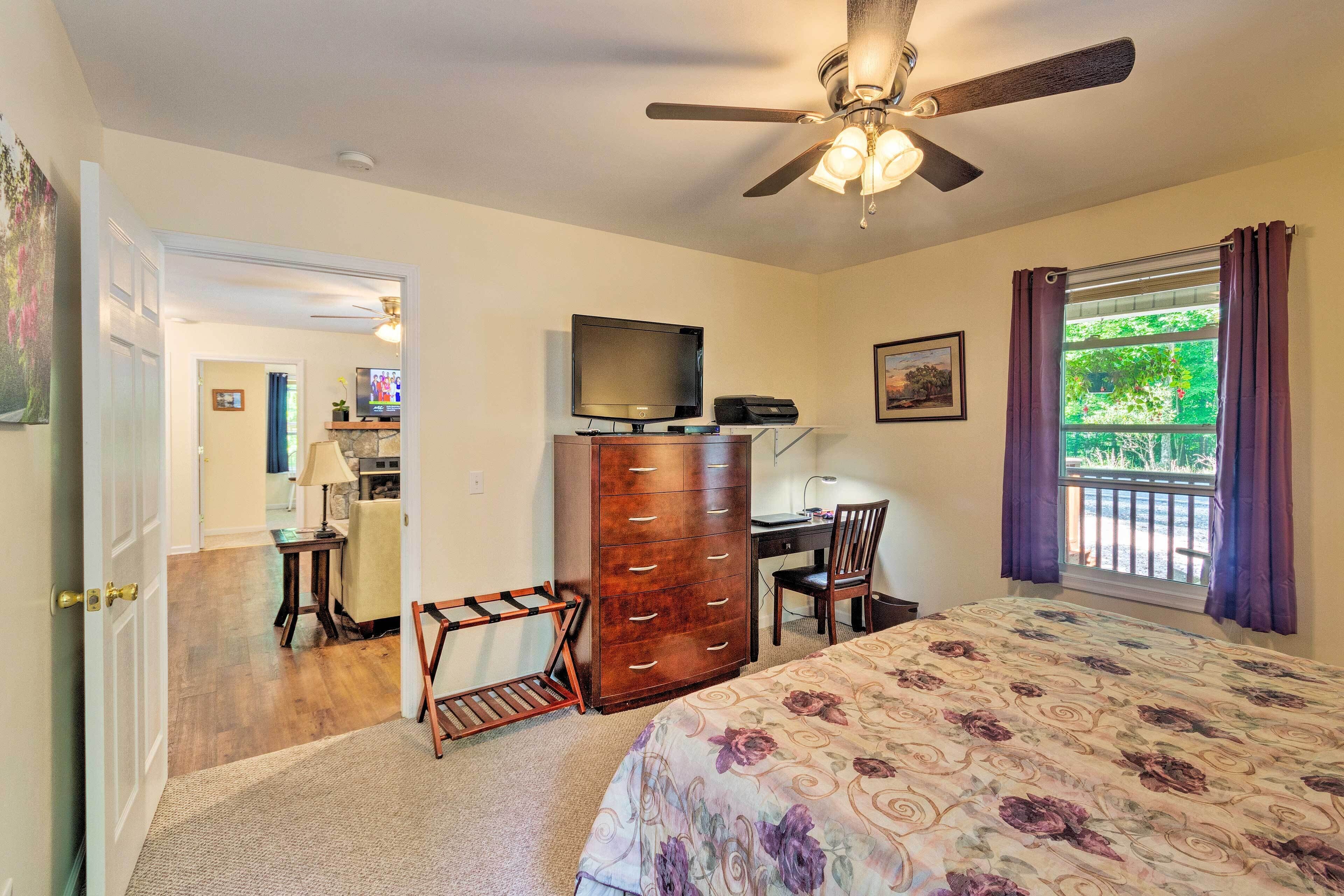 A bedroom with a bed, a dresser, a desk with a chair, a television, and a window with curtains.