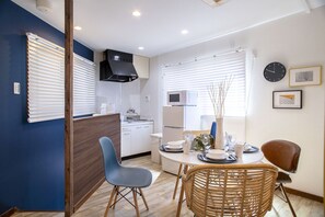 A modern kitchen with white cabinets, a black range hood, and a microwave. There is a dining table with chairs and a vase with branches. - Voyage Base Chidoribashi (Osaka)