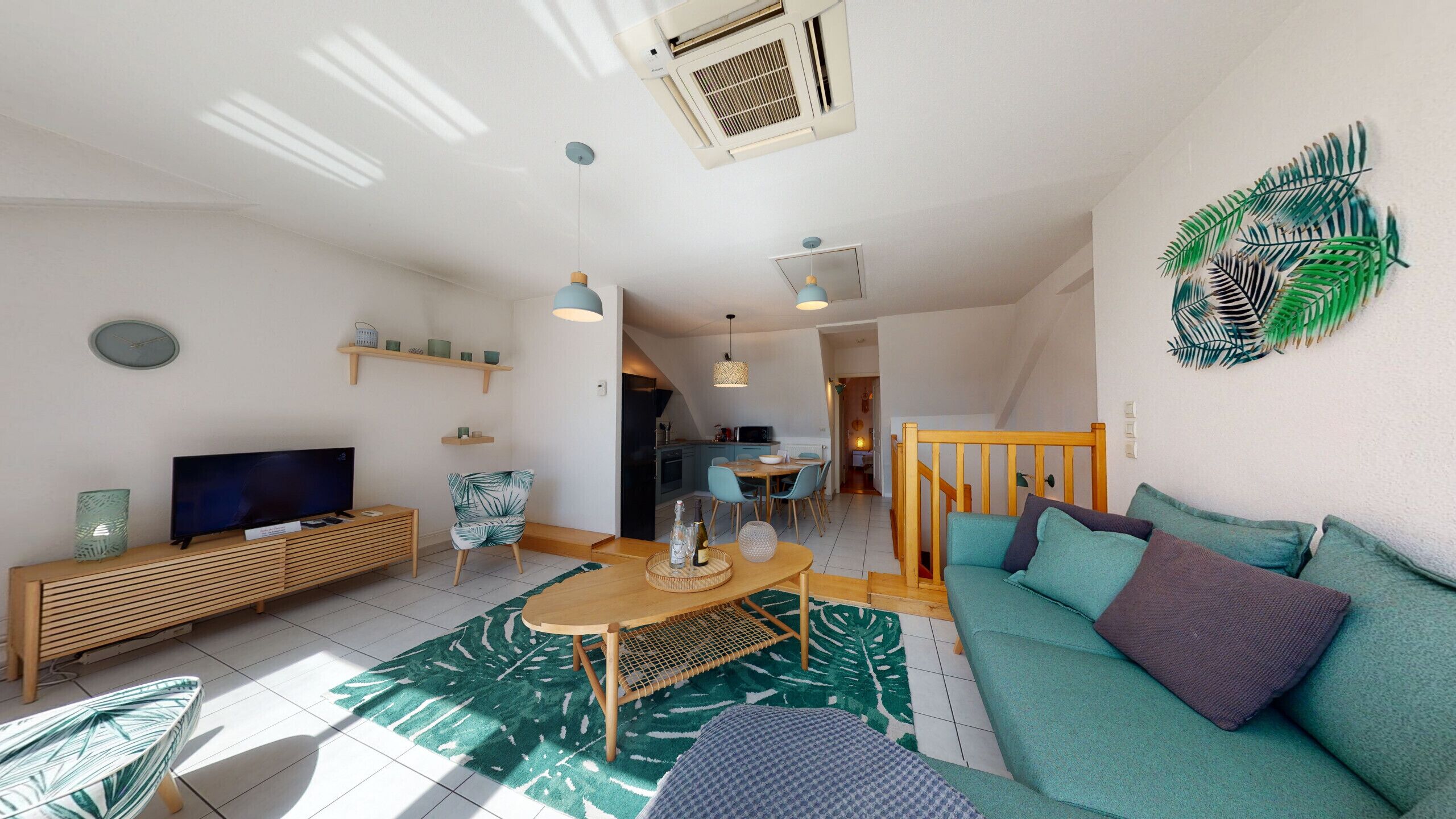 A modern living room with a sofa, TV, wooden console, and a dining area with chairs and a table.