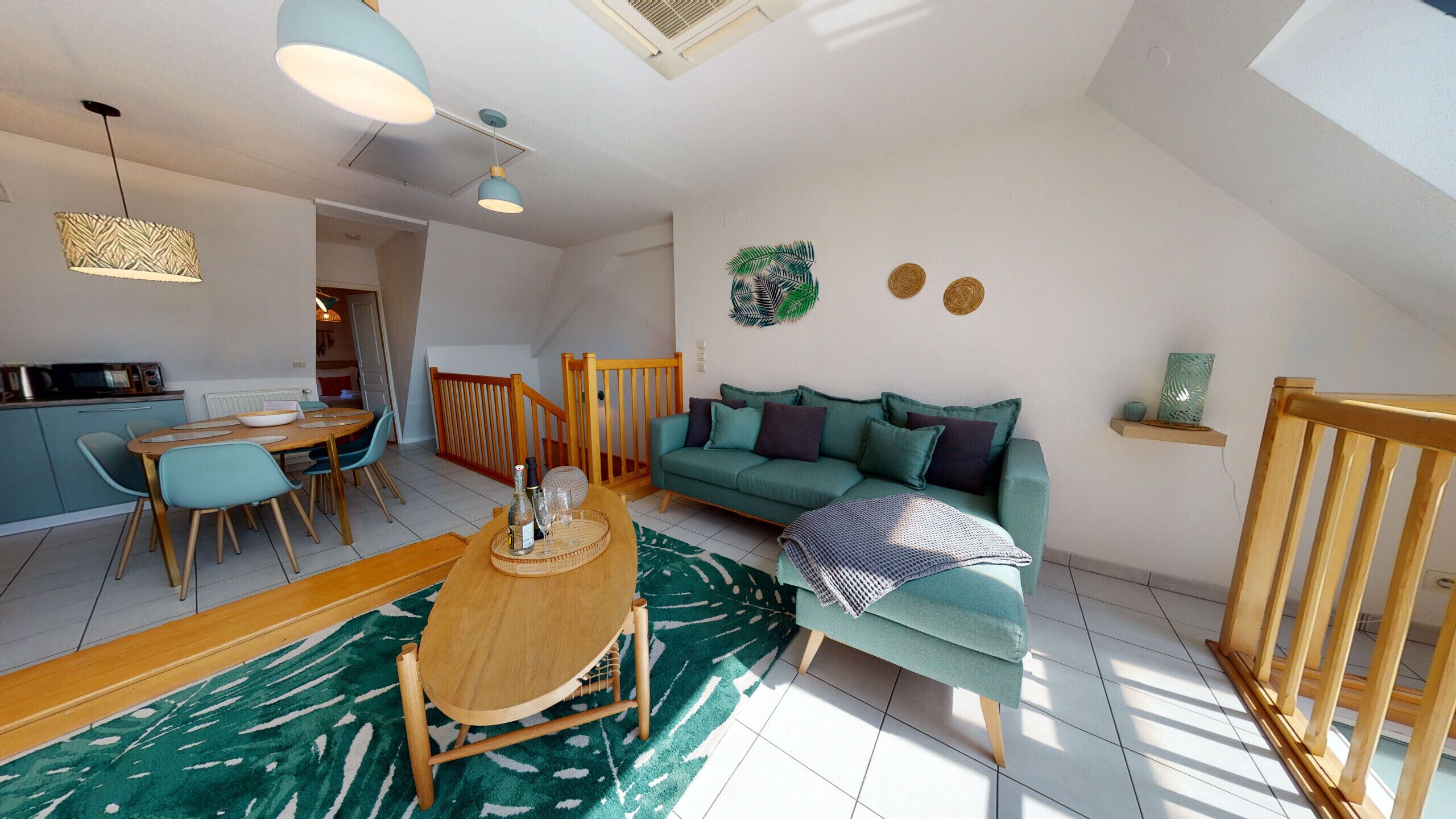 A modern living room with a sofa, dining table, and chairs, a kitchen area, and a staircase.