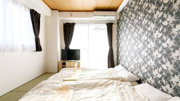 A room with two beds, a television on a wooden stand, and a window with curtains.