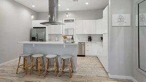 Une cuisine moderne avec des meubles blancs, un îlot central doté de tabourets, des appareils en acier inoxydable et un éclairage suspendu.
