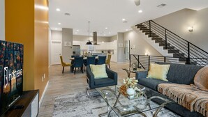Un salon moderne avec un canapé, des fauteuils et une table basse. On y trouve un escalier avec une rampe et un coin repas avec des chaises et une table.