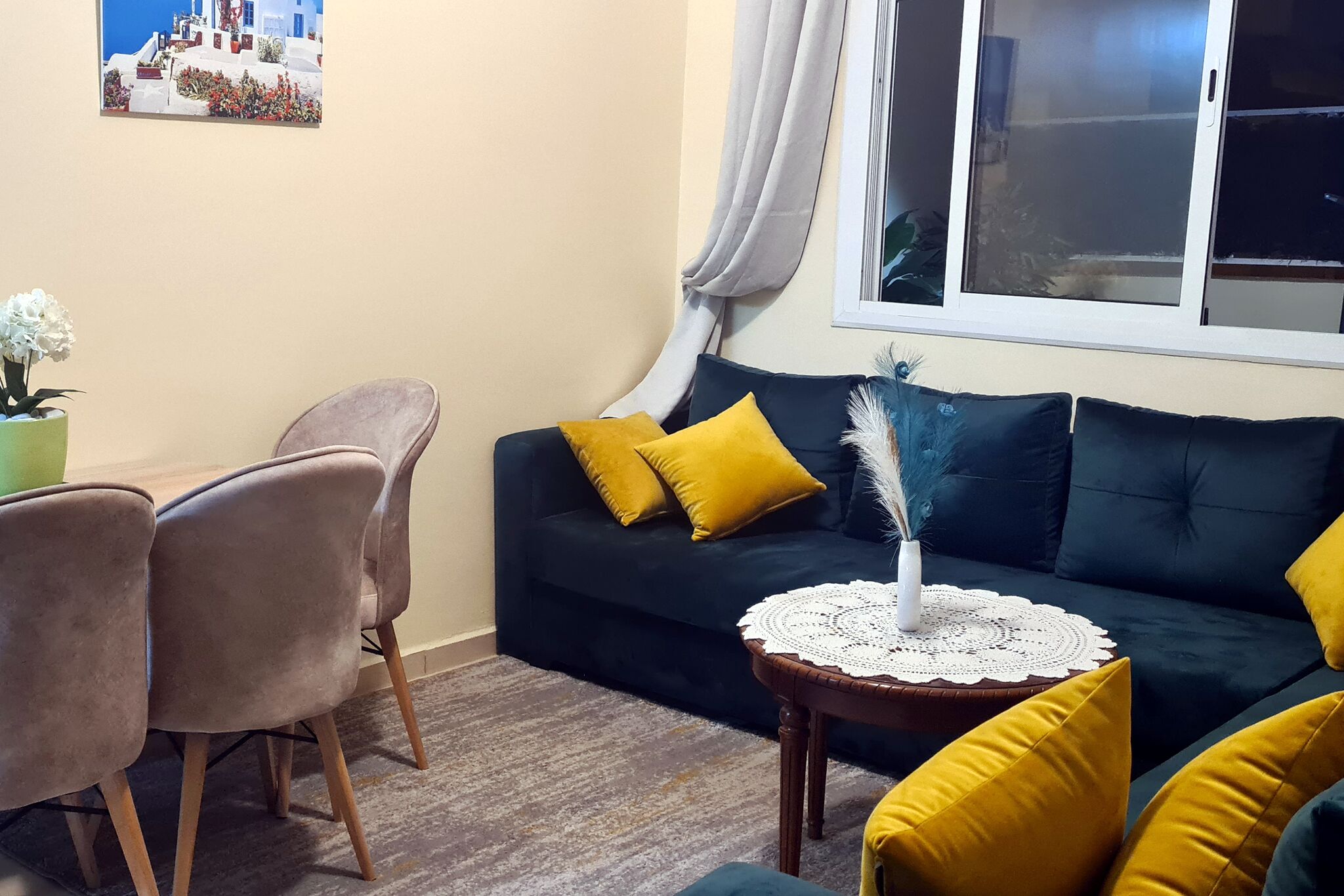 A living room with a dark blue sofa, yellow cushions, a small round table with a white doily, and a potted plant.