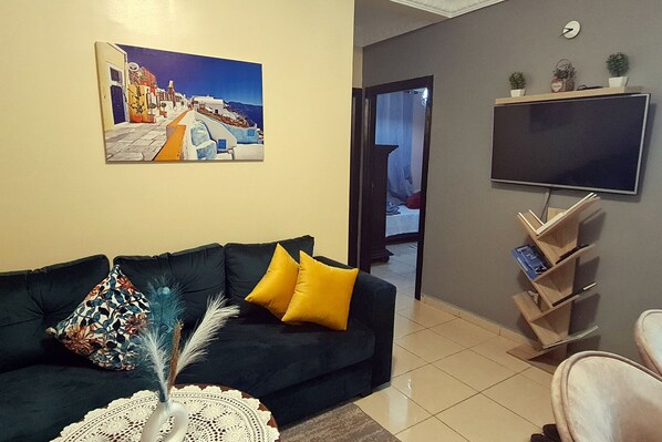 A living room with a dark sofa, a flat-screen TV, and a painting of a coastal scene.