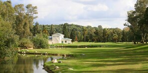 Un parcours de golf doté d’un club-house, d’un étang et entouré d’arbres.