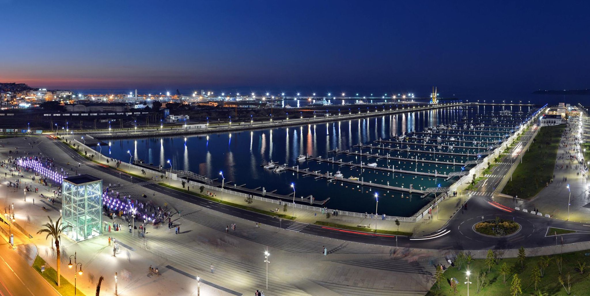 A marina with docks and boats, a pedestrian walkway, and a bridge.