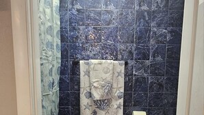 A bathroom with dark blue tiles, a white toilet, and a shower curtain with a sea turtle pattern.