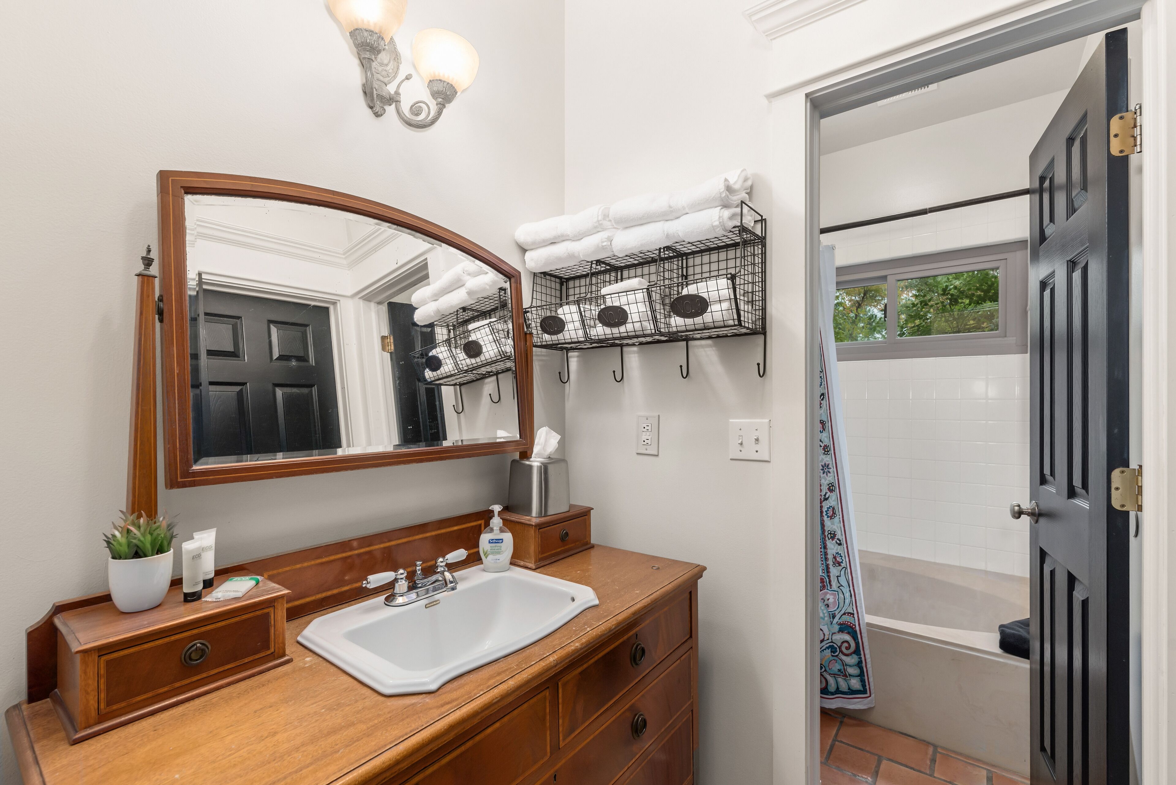 Un baño con tocador de madera, un espejo grande, un perchero y una zona de ducha.