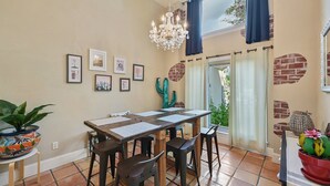 Un comedor con una mesa de madera, cuatro sillas, una araña y cuadros en la pared.