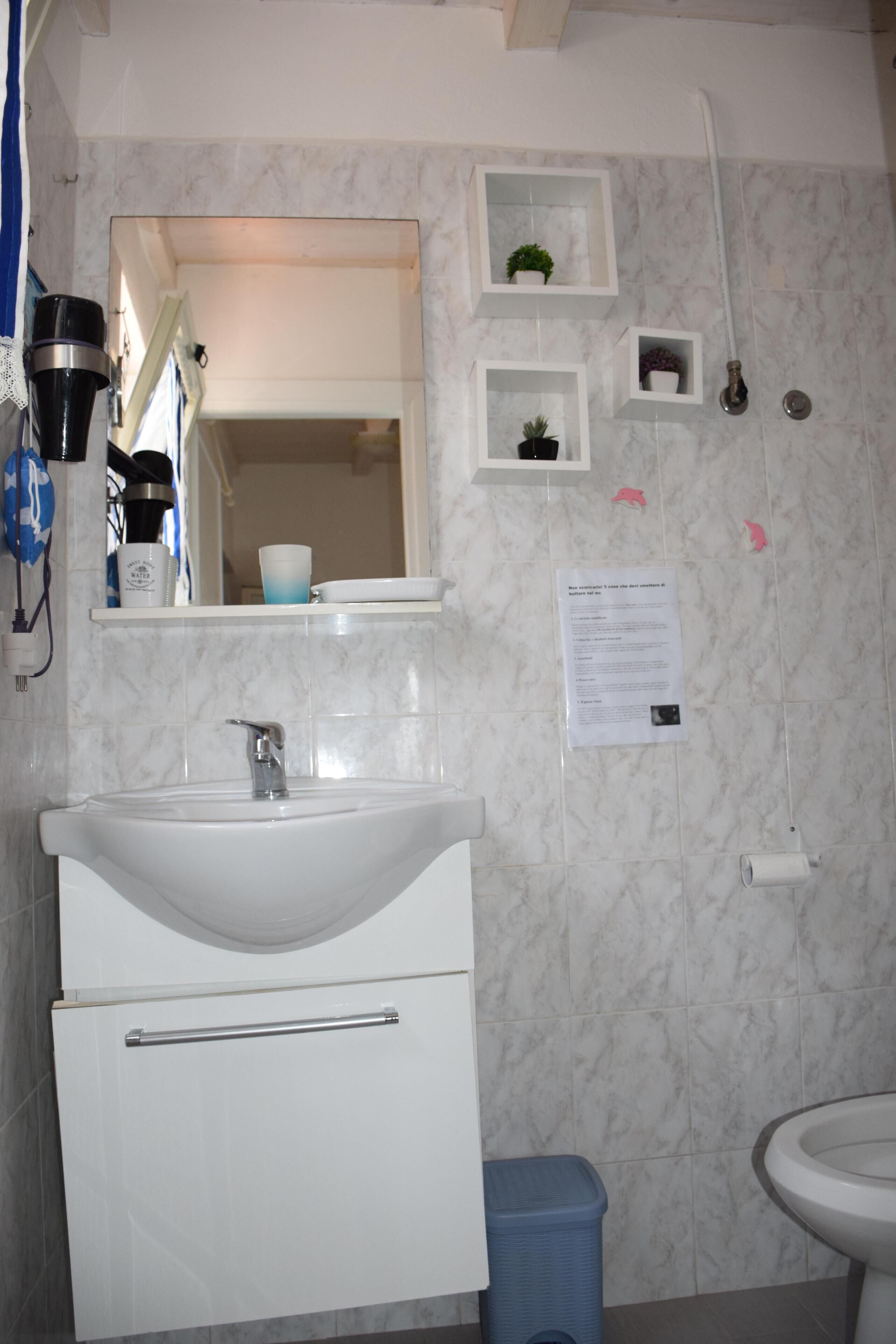 A bathroom with a white sink, mirror, and a small shelf with toiletries.