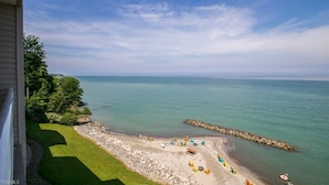 Une vue sur la plage, avec un ciel dégagé, une côte rocheuse, ainsi que plusieurs chaises de plage et parasols.