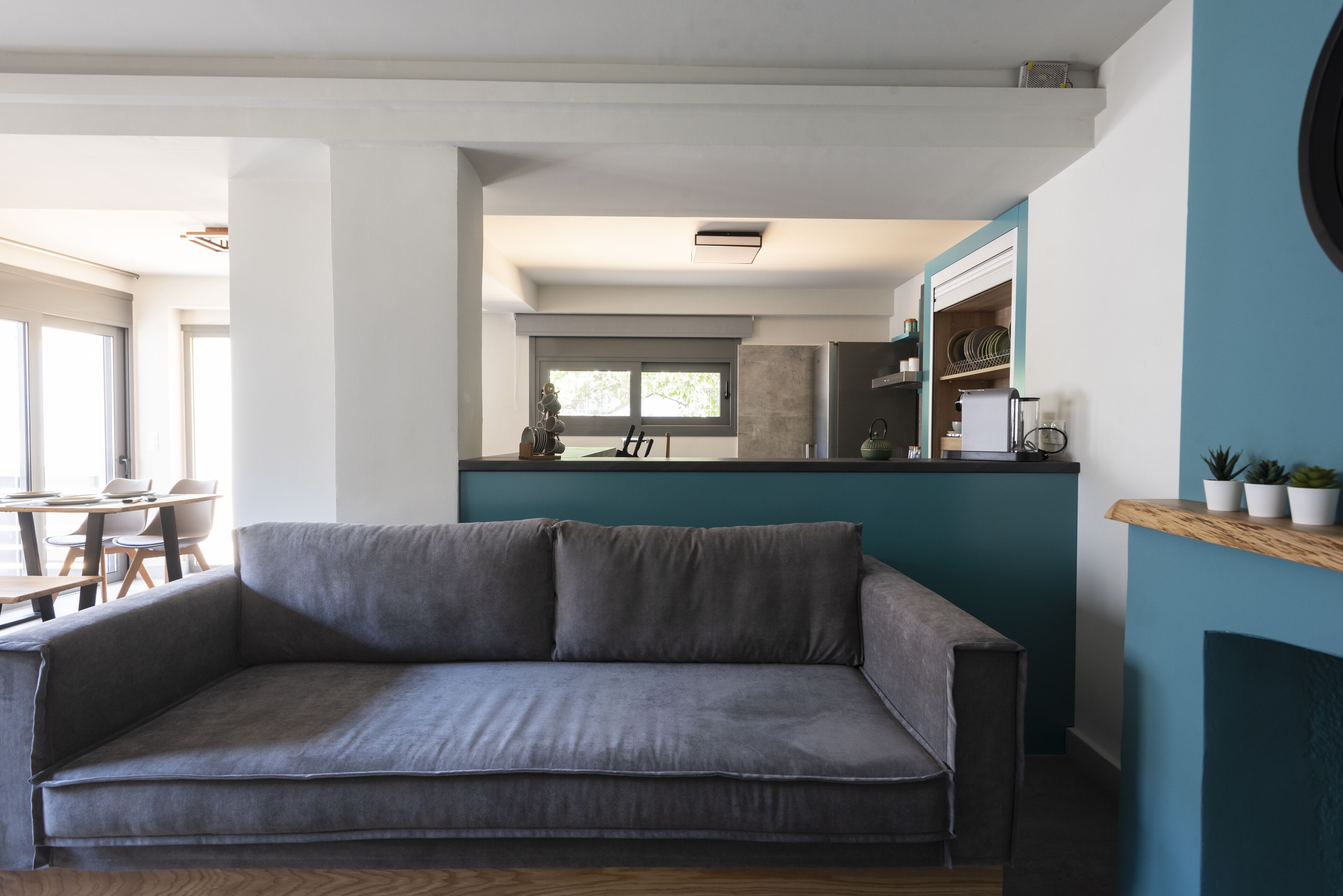 Una sala de estar moderna con un sofá gris, una mesa de centro de madera y una cocina al fondo.