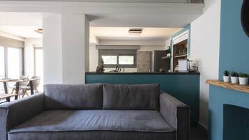 Una sala de estar moderna con un sofá gris, una mesa de centro de madera y una cocina al fondo.