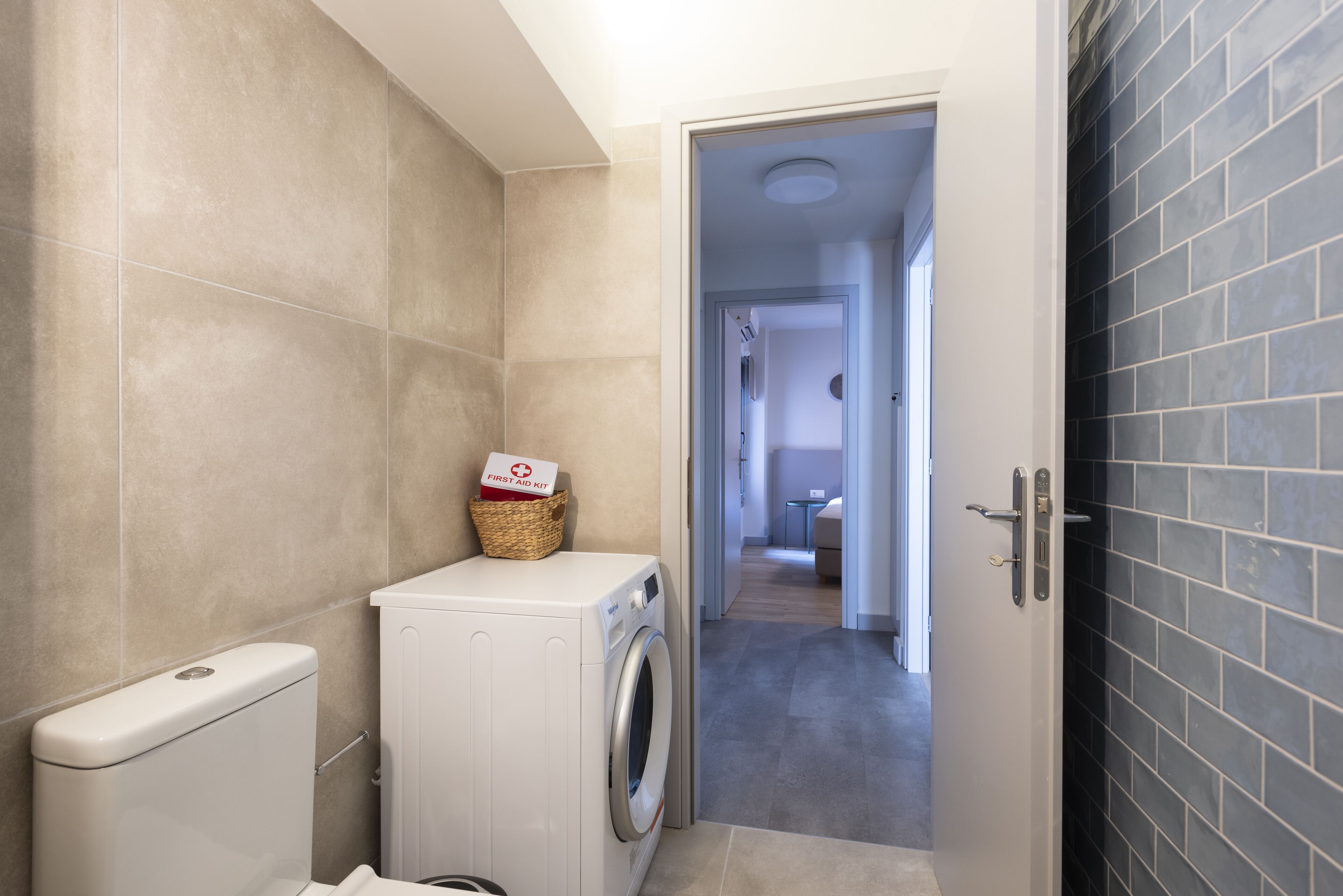 A laundry area with a washing machine and a basket labeled "First Aid Kit".